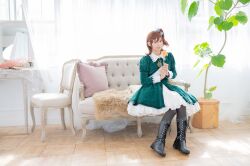  1girl black_boots boots bow brown_eyes brown_hair chair closed_mouth commentary_request cosplay cosplay_photo couch day dress english_commentary flower full_body green_dress grey_bow hair_bow hair_ornament hairclip highres holding holding_flower idolmaster idolmaster_million_live! idolmaster_million_live!_theater_days indoors jewelry kasuga_mirai kasuga_mirai_(cosplay) lace-up_boots long_sleeves looking_at_viewer medium_hair mixed-language_commentary necklace on_couch one_side_up photo_(medium) plant potted_plant real_life sitting solo voice_actor voice_actor_connection yamazaki_haruka yellow_flower 