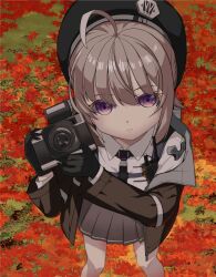  1girl ahoge autumn_leaves azuma_reiji beret black_gloves black_hat brown_hair brown_jacket camera cheyanne_(girls'_frontline_2) closed_mouth collared_shirt commentary_request day feet_out_of_frame from_above girls'_frontline_2:_exilium girls_frontline gloves grey_skirt hair_between_eyes hat holding holding_camera jacket leaf long_sleeves m200_(girls'_frontline) maple_leaf off_shoulder open_clothes open_jacket outdoors pleated_skirt shirt skirt solo standing violet_eyes white_shirt 