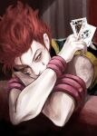  1boy card commentary_request facepaint highres hisoka_morow holding holding_card hunter_x_hunter joker_(card) king_(playing_card) korean_commentary leaning_on_object male_focus nwocp playing_card redhead short_hair sitting solo table upper_body yellow_eyes 