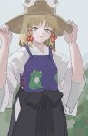  1girl adapted_costume animal_print blonde_hair cowboy_shot day frog_print grey_eyes hands_up hat highres light_smile medium_hair moriya_suwako outdoors overcast parted_lips purple_vest reisende1969 sky sleeves_past_elbows solo touhou vest wide_sleeves 