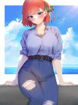  1girl arms_at_sides belt blue_eyes blue_shirt blush breasts butterfly_hair_ornament denim go-toubun_no_hanayome hair_ornament head_tilt high-waist_pants highres jeans kakato_0 large_breasts looking_at_viewer nakano_nino ocean pants parted_lips redhead shirt sitting sky solo torn_clothes torn_jeans torn_pants 