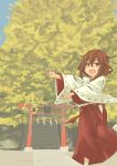  1girl absurdres alternate_costume blue_sky brown_eyes brown_hair commentary_request day fang feet_out_of_frame hakama highres inazuma_(kancolle) japanese_clothes kantai_collection miko open_mouth outdoors pot-de red_hakama ribbon-trimmed_sleeves ribbon_trim short_hair sky solo torii tree wide_sleeves 
