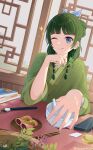  1girl artist_name blue_bow blue_eyes book bow calligraphy_brush chopsticks food green_hair green_kimono hair_bow highres holding holding_plant indoors ink japanese_clothes kimono kusuriya_no_hitorigoto licking_lips maomao_(kusuriya_no_hitorigoto) medium_hair one_eye_closed paintbrush pestle plant risdandr shogi_piece tongue tongue_out weighing_scale window 