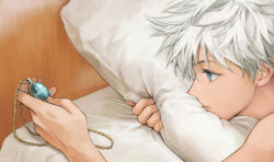  1boy bed blue_eyes closed_mouth commentary highres holding holding_jewelry holding_necklace hugging_object hunter_x_hunter jewelry killua_zoldyck kimgyunyu looking_at_object lying male_focus necklace on_stomach pillow pillow_hug short_hair solo white_hair 