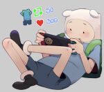  1boy adjusting_hair adventure_time animal_hood black_footwear blue_shirt blush finn_the_human green_bag grey_background highres hood lying male_focus mouth_hold nintendo_switch notkomoriisan on_back shirt shorts 