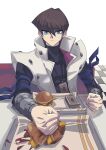  1boy absurdres artist_name black_shirt blue_eyes brown_hair burger checkered_floor clenched_hands coat covered_collarbone deck_of_cards food highres kaiba_seto looking_at_viewer male_focus medium_hair shirt sitting skmkst solo table trading_card white_coat yu-gi-oh! yu-gi-oh!_duel_monsters 