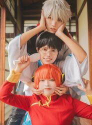  1girl 2boys absurdres aburanaka_tane arms_up black_hair blue_eyes blunt_bangs brown_eyes bun_cover cheek_pinching cheek_pull cheek_squash chinese_clothes comb commentary_request cosplay cosplay_photo double_bun emoemocos gintama glasses grin hair_bun hands_on_another's_cheeks hands_on_another's_face hands_up head_on_head head_rest highres holding holding_comb indoors japanese_clothes kagura_(gintama) kagura_(gintama)_(cosplay) kimono lips long_sleeves looking_at_viewer multiple_boys orange_hair parted_lips photo_(medium) photoshop_(medium) pinching red_eyes sakata_gintoki sakata_gintoki_(cosplay) shimura_shinpachi shimura_shinpachi_(cosplay) short_hair smile tangzhuang teeth white_hair wide_sleeves yusura_uni 