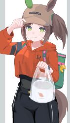  1girl absurdres animal_ears bag baseball_cap black_pants breasts brown_hair closed_mouth commentary_request crop_top crop_top_overhang cropped_hoodie ear_covers ears_through_headwear green_bag green_eyes hair_through_headwear hat highres holding hood hoodie horse_ears horse_girl horse_tail ines_fujin_(casual)_(umamusume) ines_fujin_(umamusume) insulated_delivery_bag long_sleeves looking_at_viewer onigiri_noe orange_hoodie pants plastic_bag side_ponytail single_ear_cover smile solo tail umamusume 
