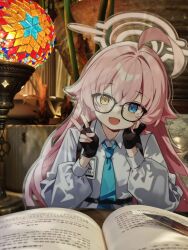  1girl :d acrylic_stand_(medium) ahoge bespectacled black-framed_eyewear black_gloves blue_archive blue_eyes blue_necktie blush book chinese_commentary collared_shirt commentary_request commission fang fingerless_gloves glasses gloves hair_between_eyes halo head_rest heterochromia highres hoshino_(blue_archive) huge_ahoge long_hair long_sleeves looking_at_viewer merchandise mo_zi_de_kuai_le_sheng_huo necktie open_mouth photo_(medium) pink_hair pink_halo puffy_long_sleeves puffy_sleeves shirt smile solo straight-on upper_body v white_shirt yellow_eyes 